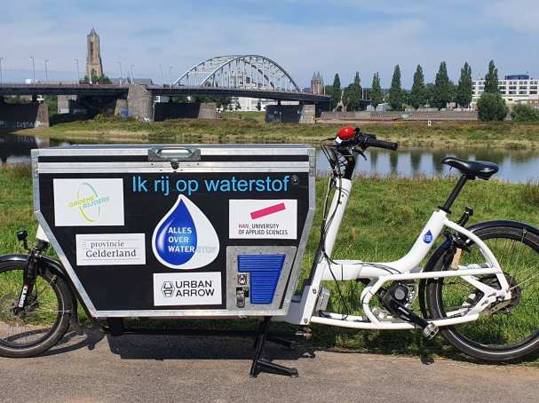 316650 Waterstofbakfiets met natuur, rivier en John Frostbrug Arnhem op de achtergrond