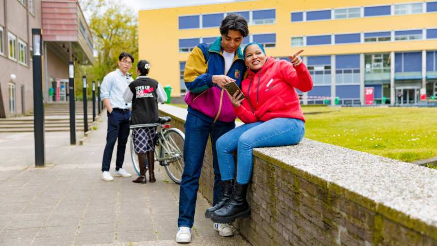 ae5d82fe-5974-11ee-90b0-024215b4a989 Chadionne pointing at something, Diego pointing at something on a smartphone and two other students by the bicycle in the background at Arnhem Campus.