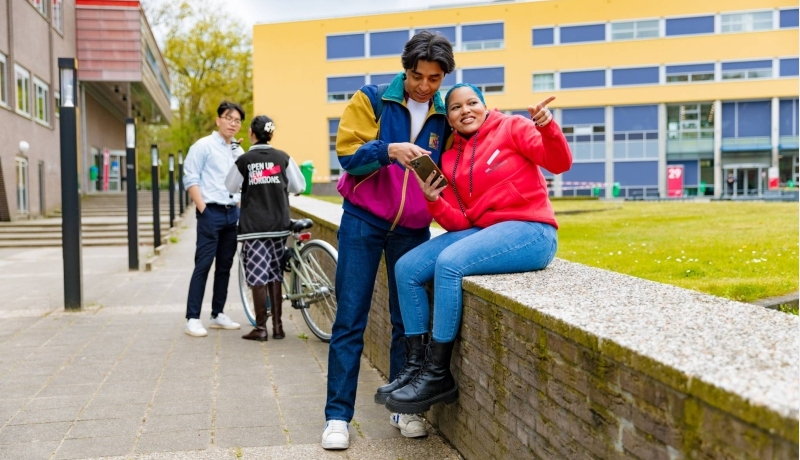 Chadionne pointing at something, Diego pointing at something on a smartphone and two other students by the bicycle in the background at Arnhem Campus.