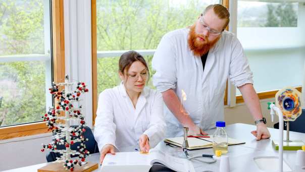 Twee Leraar Biologie studenten kijken vragen in het biologieboek. Ze hebben een labjas aan.