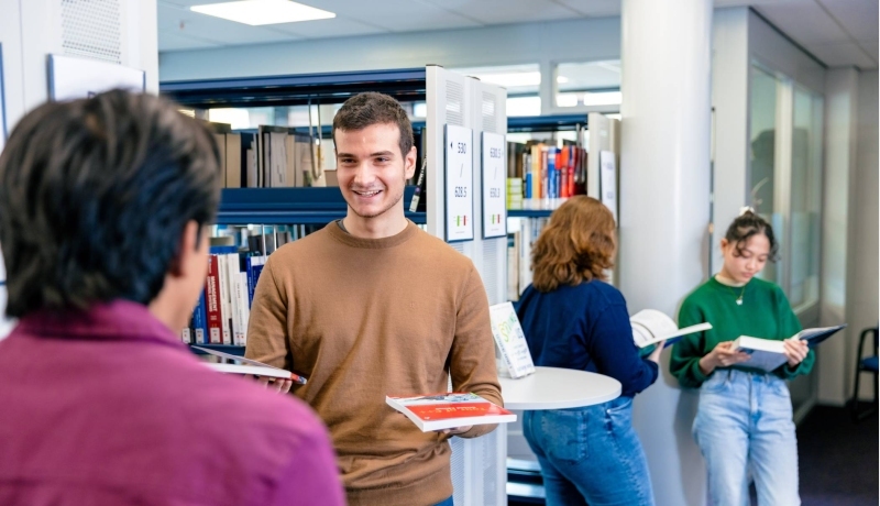 International students Diego, Andrei, Noa and Tam browsing through books in the library on the Arnhem campus of HAN University of Applied Sciences.