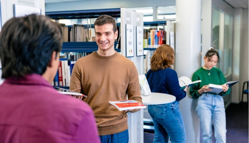International students Diego, Andrei, Noa and Tam browsing through books in the library on the Arnhem campus of HAN University of Applied Sciences.
