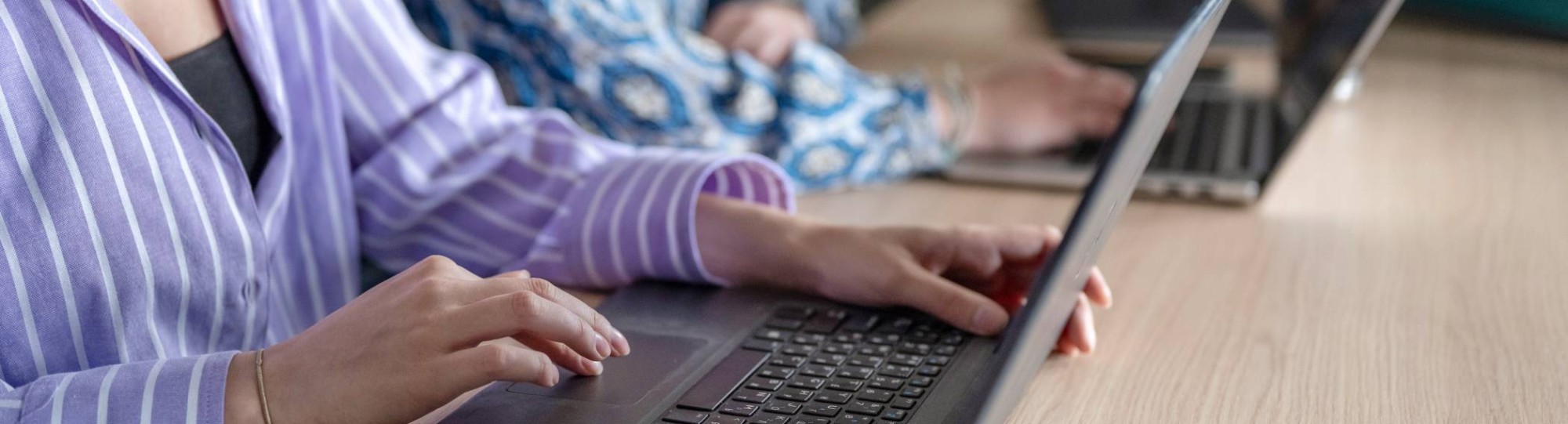 Twee laptops van studenten die aan het typen zijn, in de klas. 