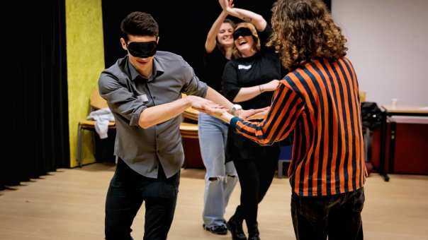Vier personen in een danslokaal die met een zwarte blinddoek hand in hand met elkaar dansen