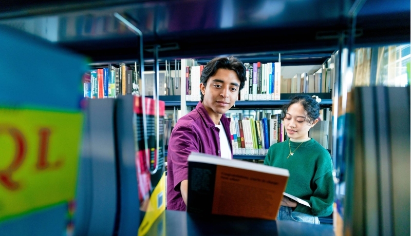 International students Diego and Tam looking for books in the library on the Arnhem campus of HAN University of Applied Sciences.