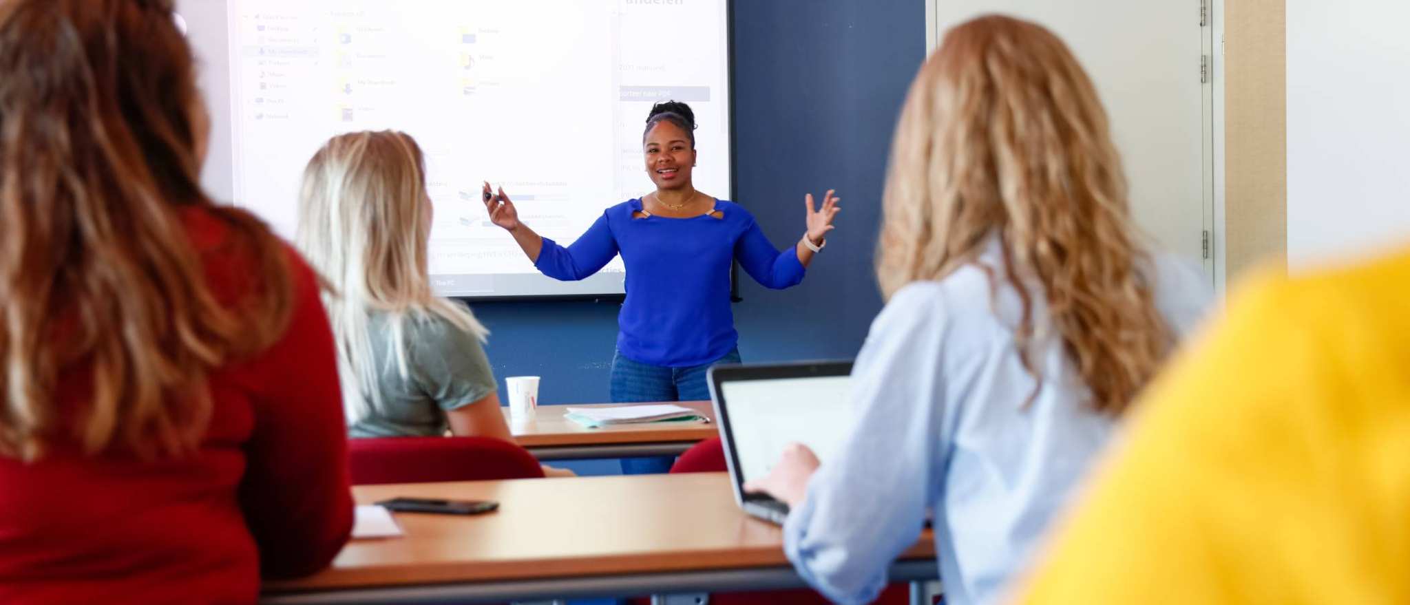 HBO master studenten geven een presentatie bij het scherm voor in de klas, andere studenten luisteren