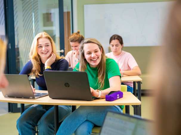 Studenten tijdens theorieles lachend achter laptops