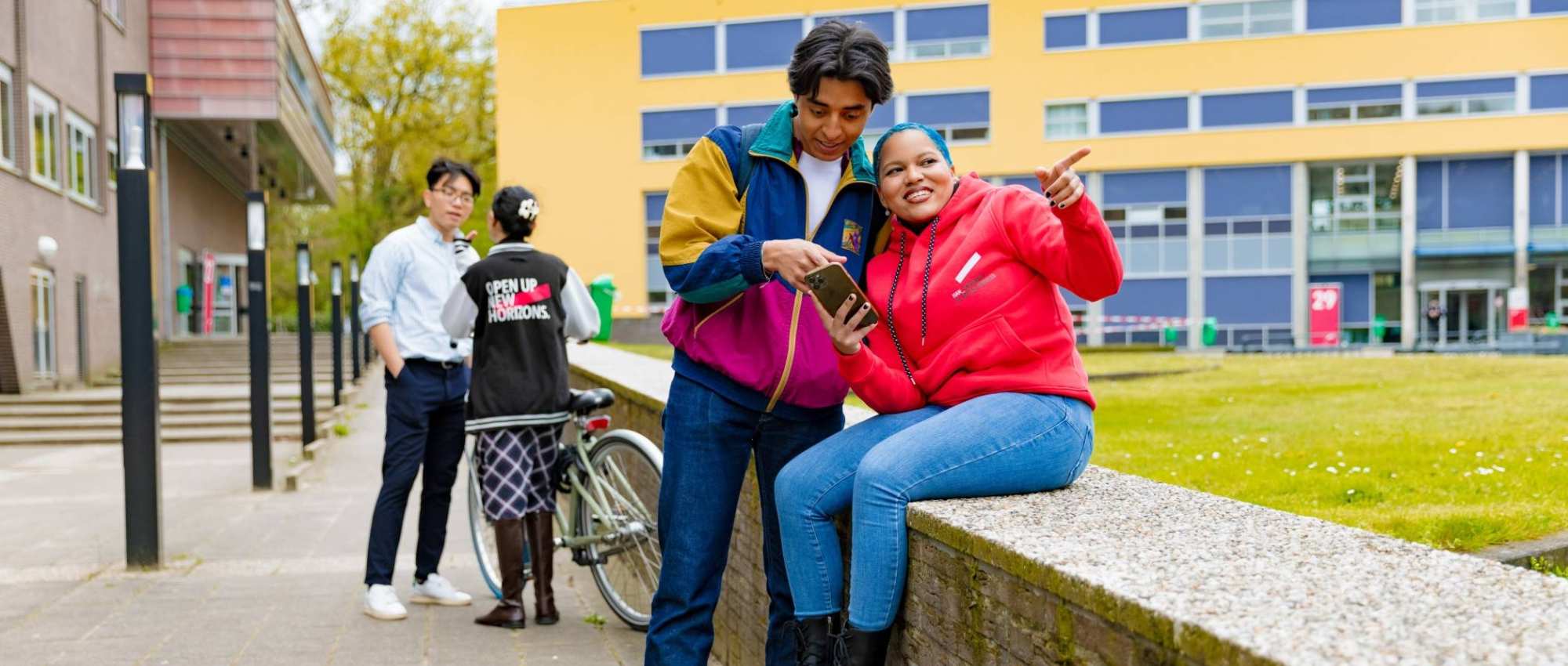 Chadionne pointing at something, Diego pointing at something on a smartphone and two other students by the bicycle in the background at Arnhem Campus.