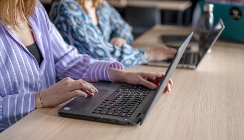 Twee laptops van studenten die aan het typen zijn, in de klas. 
