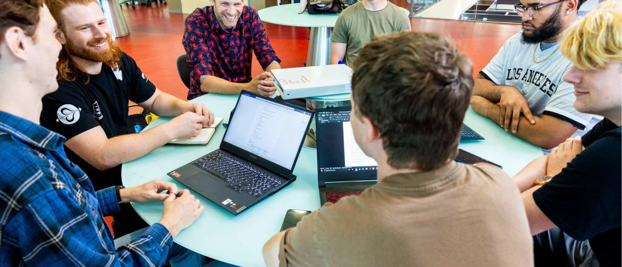 a group of engineering students -mechanical werktuigbouwkunde - working on a project together at a round table with laptops