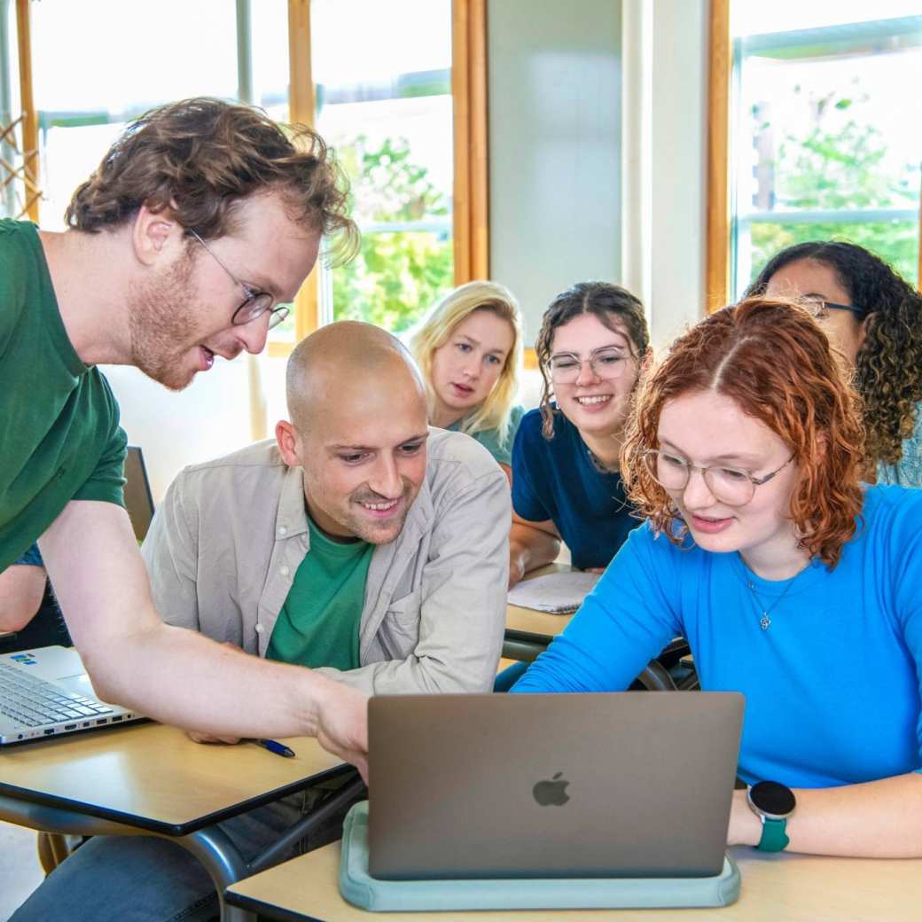 Teacher is pointing at laptop in front of students