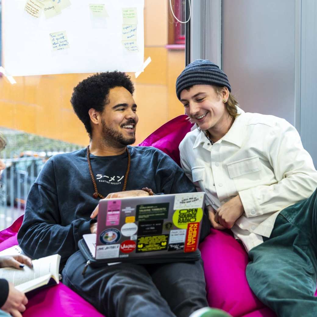 Two boys on a pink beanbag look at a laptop.