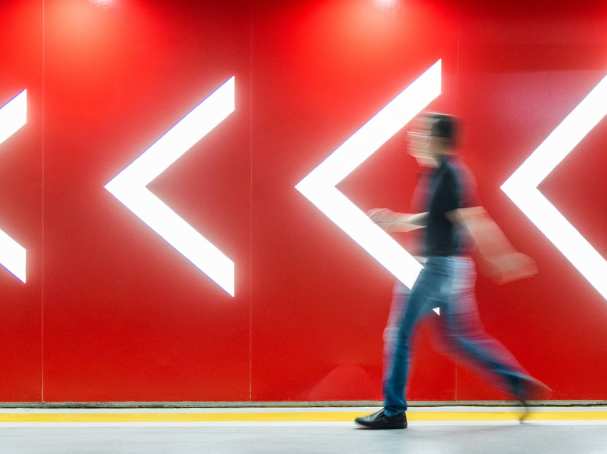Man loopt met de richting mee voor rode wand met lichtgevende peilen. 