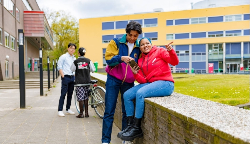 Chadionne pointing at something, Diego pointing at something on a smartphone and two other students by the bicycle in the background at Arnhem Campus.