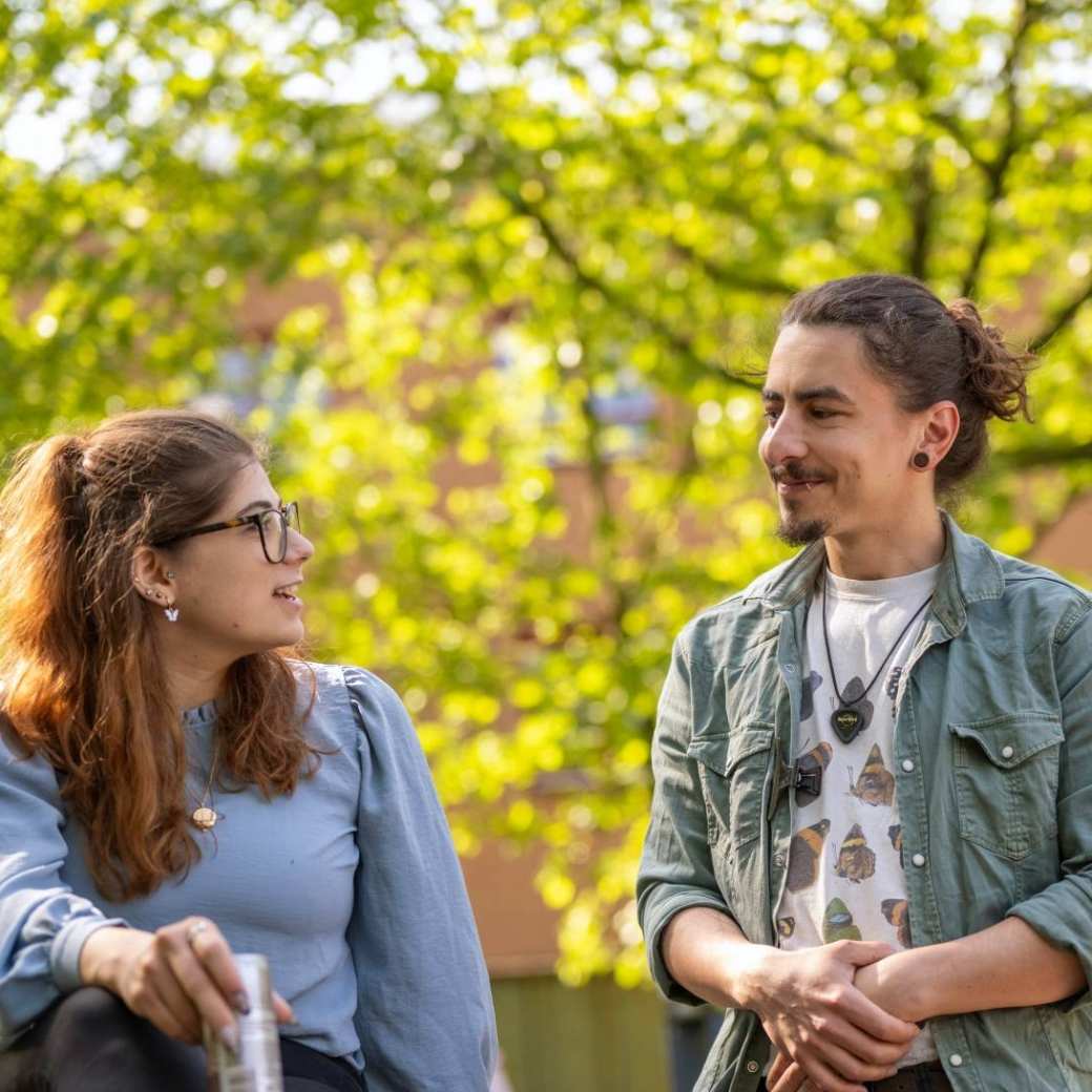 Twee studenten lachen naar elkaar, zijn buiten bij K33.