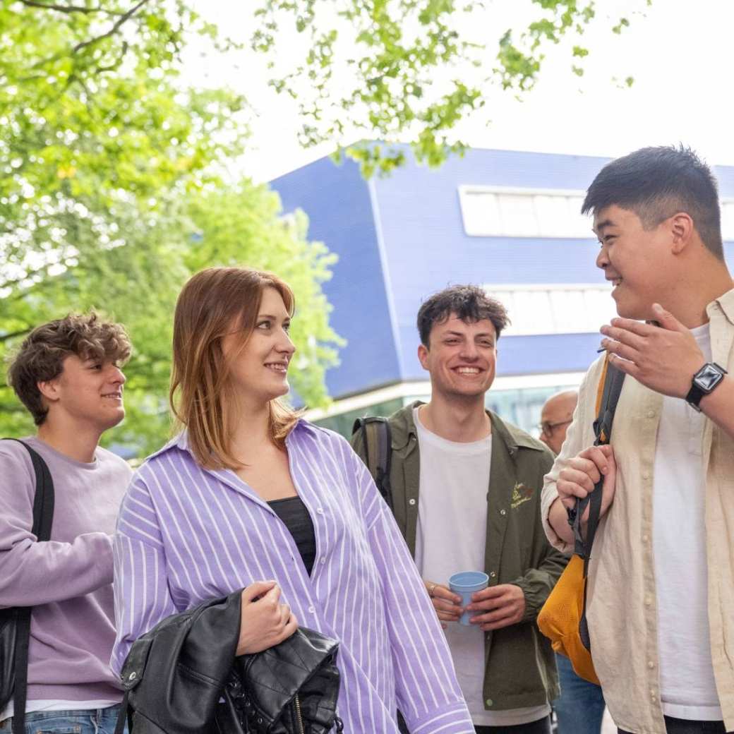 Groepje studenten staan buiten, met elkaar aan het kletsen, op de campus.