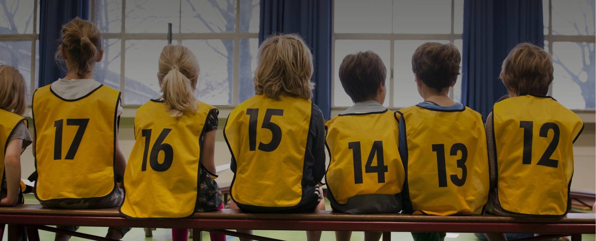 Kinderen in een gymzaal met hesjes aan op de rug gefotografeerd