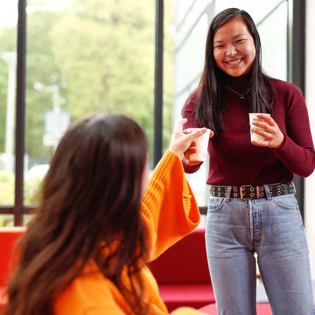 Student bij rode banken geeft koffie aan andere student