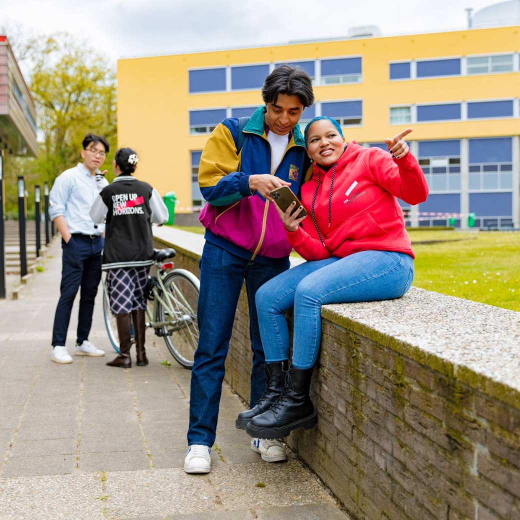 Chadionne pointing at something, Diego pointing at something on a smartphone and two other students by the bicycle in the background at Arnhem Campus.